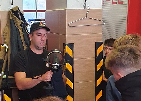 Strażak- sekc. A. Chołka, prezentuje uczniom działanie strażackiej maski ochrony układu oddechowego