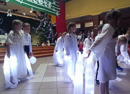 dziewczynki ubrane na biało tańczą ze świecącymi szarfami, chłopcy stoją z lampionami