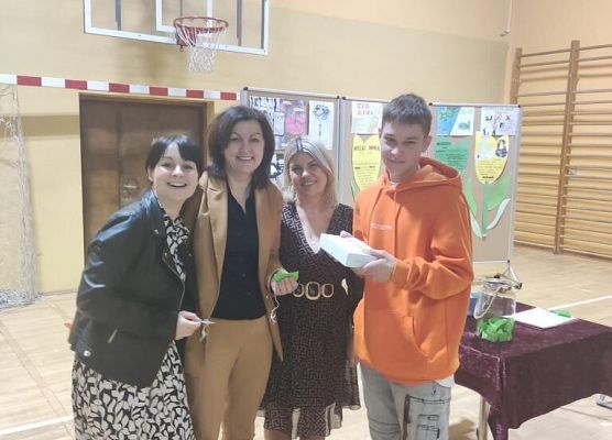 Uczeń w pomarańczowej bluzie , kobieta w beżowym komplecie ,dwie kobiety w sukienkach pozują do zdjęcia.