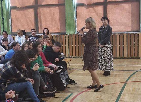 Kobieta mówi przez mikrofon do grupy uczniow.