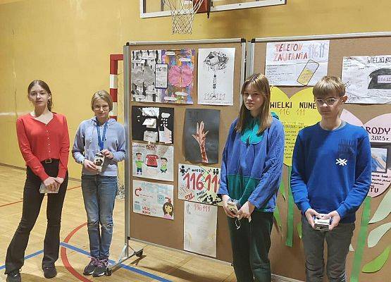 Kobiety wręczają nagrody uczniom. Uczniowie stoją z nagrodami przy tablicy z plakatami.