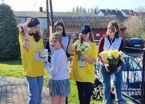 Uczennice w żółtych koszulkach trzymają w ręce puszkę i żółte kwiaty.