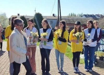 Uczennice w żółtych koszulkach  stoją jedna obok drugiej , trzymają w rękach żonkile.