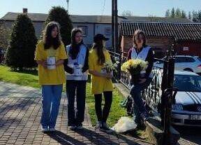 Uczennice w żółtych koszulkach trzymają w ręce puszkę i żółte kwiaty.