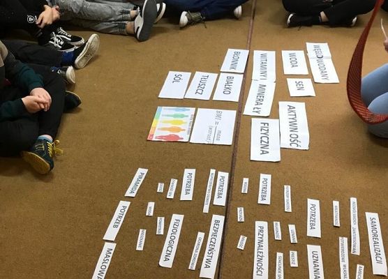 Uczniowie patrzą na leżące na dywanie kartki.