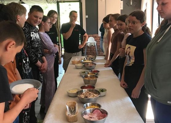 Uczniowie stoją przy stole. Na stole leżą miski z jedzeniem .