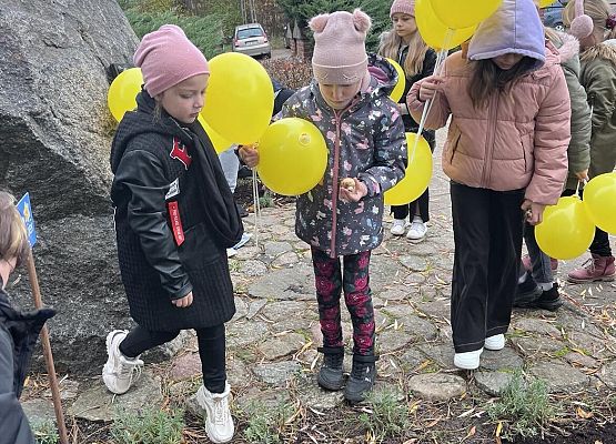 Uczniowie trzymają żółte balony i sądzą cebulki żonkili