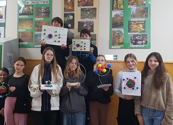 Grupa dzieci z klasy 7a prezentuje model budowy atomu.