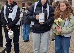 Uczniowie przed kościołem. W rękach trzymają puszki na pieniądze i żonkile