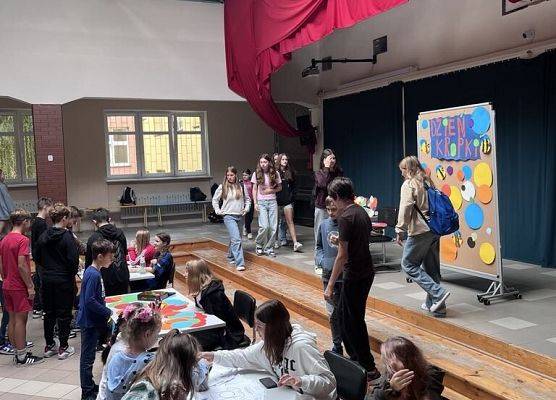 Grupa uczniów na dużej sali, zgromadzona przy stolikach.