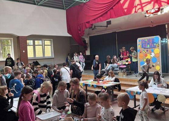 Grupa uczniów stoi na dużej sali przy stolikach