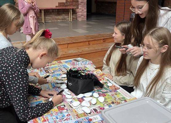 Na stoliku leżą kamienie i flamastry, uczniowie malują na nich