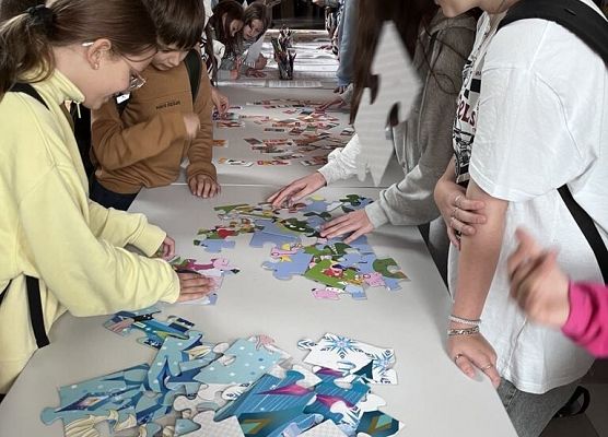 Na stole leżą ogromne puzzle , uczniowie układają je