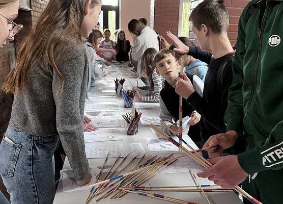 Przy dużym stole stoją uczniowie , na stołach leżą różne rzeczy do wykonywania zadań