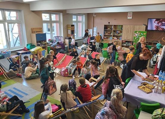 Uczniowie siedzą na leżakach , na stole leżą ciastka i soki.