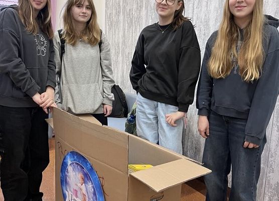 Uczniowie stoją przy kartonie z hasłem Paczuszka dla Maluszka i pozują do zdjęcia