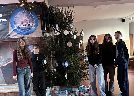 Uczniowie stoją przy choince i pozują do zdjęcia.