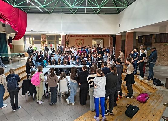 Na środku patio siedzą i stoją uczniowie , którzy zgromadzili się aby debatować