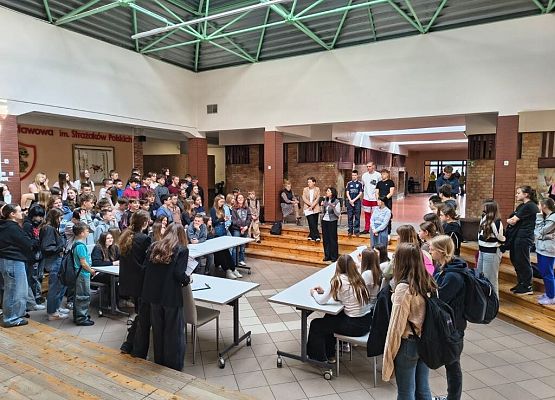 Na środku patio siedzą i stoją uczniowie , którzy zgromadzili się aby debatować