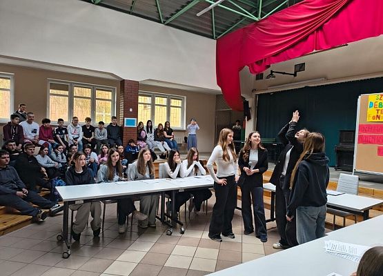 Na środku patio stoją uczniowie, rzucają monetą