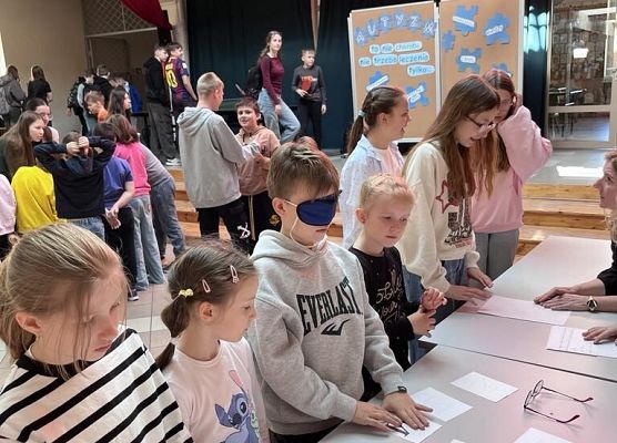 Uczniowie stoją przy stolikach i wykonują zadania