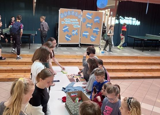 Uczniowie stoją przy stolikach i wykonują różne zadania