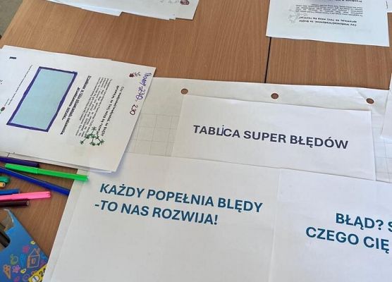 Na stole leżą kartki z zadaniami dla uczniów. Uczniowie wypełniają je mazakami