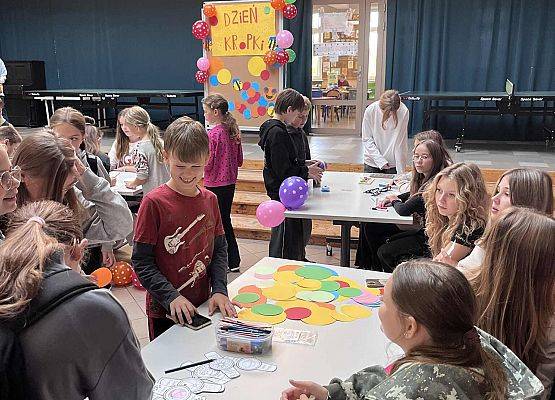 Uczniowie siedzą przy stoliku i rysują na kolorowych kropkach