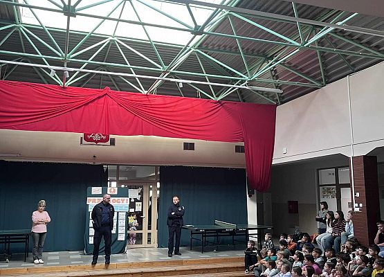 Uczniowie siedzą na patio szkoły i wysłuchują pogadanki z policjantami