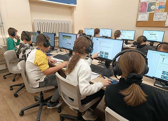 dzieci ze słuchawkami rozwiązują zadania w pracowni komputerowej