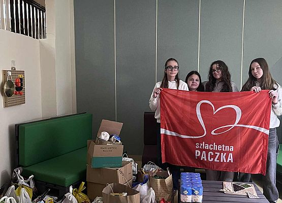 Uczniowie trzymają plakat czerwony z napisem Szlachetna paczka obok są dary